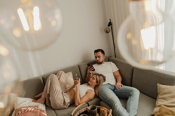 Couple Relaxing on Sofa at Home Using Smartphones with Snacks Nearby © blackday