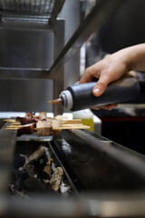 chef echando salsa a unas brochetas de carne y pulpo que se brasean en el horno