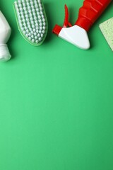 Flat lay of various cleaning supplies on green background. Includes brush, sponge, spray bottle,...