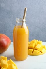 Tasty mango juice in glass bottle and fresh fruits on white table