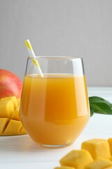 Tasty mango juice in glass, fresh fruits and green leaves on white wooden table, closeup