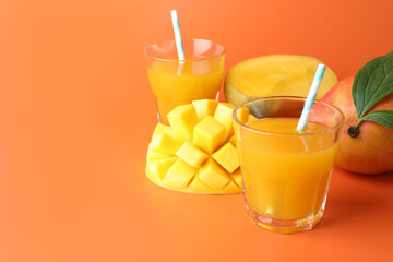 Tasty mango juice in glasses and fresh fruits on orange background, closeup. Space for text