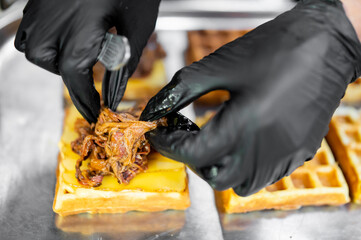 Close-up of a gloved chef placing pulled meat on a waffle with melted cheese, showcasing gourmet...