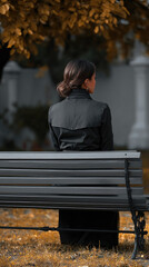 Fototapeta premium Woman in black coat sitting on park bench, autumn leaves, peaceful outdoor scene, rear view, solitude, thoughtful mood