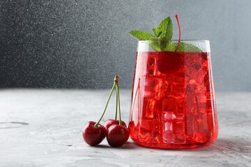 Tasty cherry soda with ice cubes, berries and mint on grey textured table, closeup. Space for text