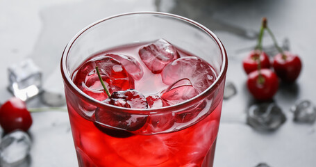 Tasty cherry soda with ice cubes and berry in glass on grey table, closeup