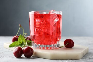 Tasty cherry soda with ice cubes, berries and mint in glass on grey textured table, closeup