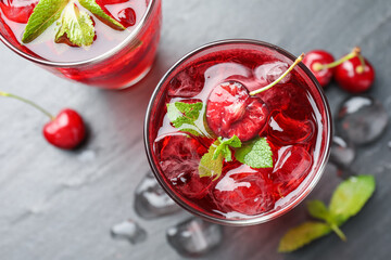 Tasty cherry soda with ice cubes, berries and mint in glasses on grey table, flat lay