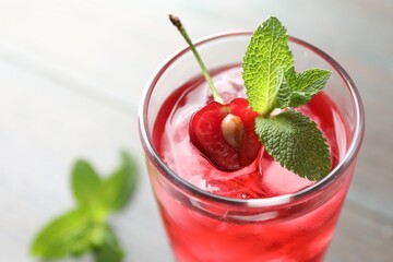 Tasty cherry soda water with ice cubes, berry and mint in glass on light table, closeup