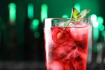 Tasty cherry soda water with ice cubes, berry and mint in glass on blurred green background, closeup