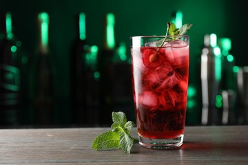 Tasty cherry soda water with ice cubes, berry and mint in glass on wooden table against blurred green background, closeup. Space for text
