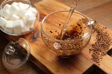 Pouring hot water into cup with instant coffee on wooden table, closeup
