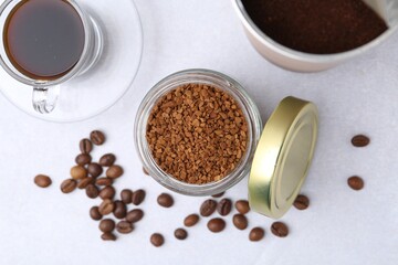 Instant coffee in jars, beans and hot drink on light grey table, flat lay