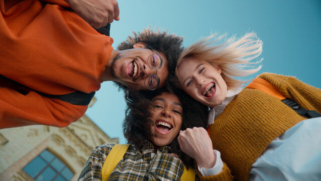 Bottom views three multiracial students together in city university leaning heads African American man male guy Caucasian women girls females celebrate success education winners gesture looking down