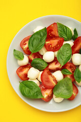 Italian Caprese salad with cherry tomatoes, mozzarella, basil on plate on yellow background. Vertical photo