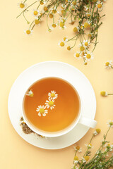 Aromatic herbal tea in white cup and chamomiles on beige background. Vertical photo