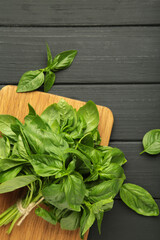 Green basil herb on cutting board on black background. Vertical photo