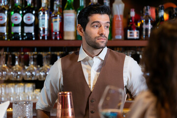 Close-up portrait of a handsome, attentive young bartender with a beard, wearing a vest and...