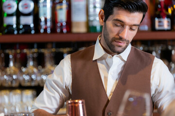 Close-up portrait of a handsome, attentive young bartender with a beard, wearing a vest and listening to an order at a classic bar. Professional service in a restaurant.
