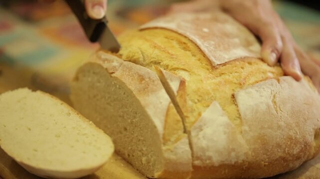 P&atilde;o italiano redondo sendo cortado por m&atilde;os femininas usando uma faca de serra em camera lenta ou slow motion.