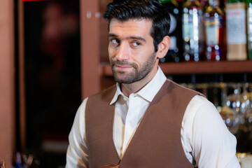 Close-up portrait of a handsome, attentive young bartender with a beard, wearing a vest and...