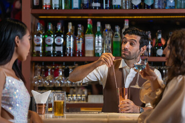 Expatriate bartender skillfully preparing cocktails for two beautiful female customers at a stylish bar counter in Bangkok, Thailand. Warm atmosphere and friendly service in a vibrant city.