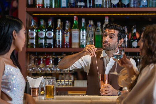 Expatriate bartender skillfully preparing cocktails for two beautiful female customers at a stylish bar counter in Bangkok, Thailand. Warm atmosphere and friendly service in a vibrant city. - Powered by Adobe