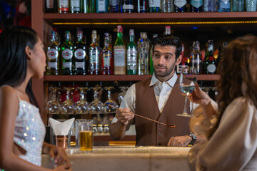 Expatriate bartender skillfully preparing cocktails for two beautiful female customers at a stylish bar counter in Bangkok, Thailand. Warm atmosphere and friendly service in a vibrant city.