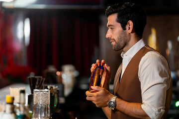 A handsome and focused professional bartender concentrating as he prepares a craft cocktail with a copper shaker in a stylish, dark bar at night.