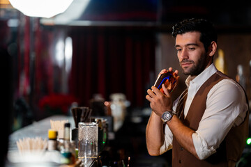 A handsome and focused professional bartender concentrating as he prepares a craft cocktail with a copper shaker in a stylish, dark bar at night.