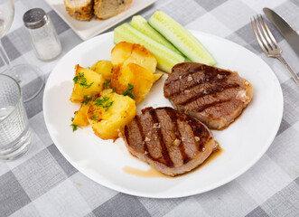 Juicy beef steak with potatoes, served with cucumber and herbs