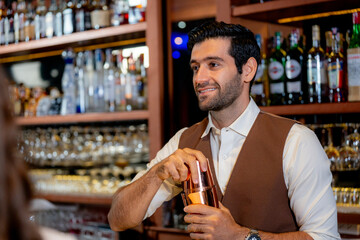 Friendly handsome bartender smiling and talking with a customer while preparing a craft cocktail with a copper shaker. Excellent hospitality and service in a modern lounge at night.