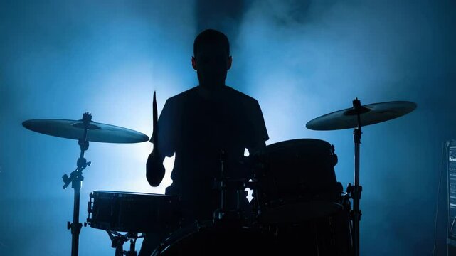 A silhouette drummer creates a rhythm on stage amidst dramatic lighting, with cymbals and drums highlighted by smoke.