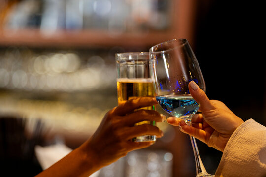 Two female friends raising glasses of beer and a blue cocktail for a toast in a stylish bar. Concept of celebration, friendship, and happy hour on a night out in Bangkok.