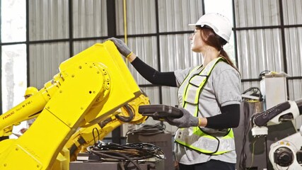 Female robot engineer holding an analog controller inspects the robot's hydraulic welding equipment during maintenance and safety check before controlling the system and programming the robot to work. - Powered by Adobe