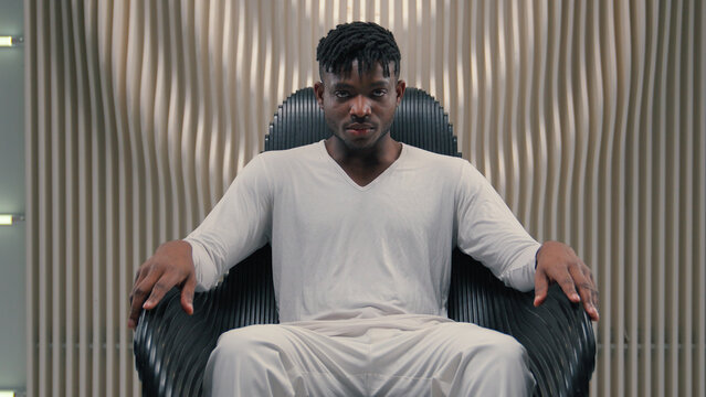Futuristic confident serious gamer programmer hacker African American man guy male sitting in chair in futurism modern room studio in chair looking at camera 3D computer graphics AI network concept