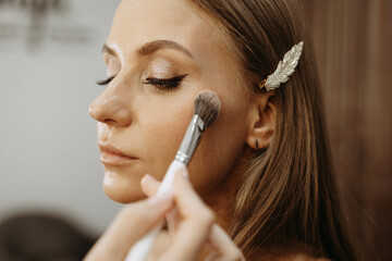 Makeup artist applying blush or highlighter to model face. Close-up