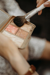 Makeup artist dipping brush into highlighter palette. Close-up vertical