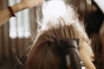 Makeup artist hairdresser combing hair of female model with comb and hair dryer. Close-up view