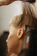 Makeup artist hairdresser combing hair of female model with comb and hair dryer blow. Close-up vertical