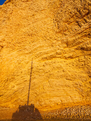Sunlit golden sandstone cliff face with layered sedimentary rock and a long shadow cast across it. Koufonisia Islands, Cyclades, Greece