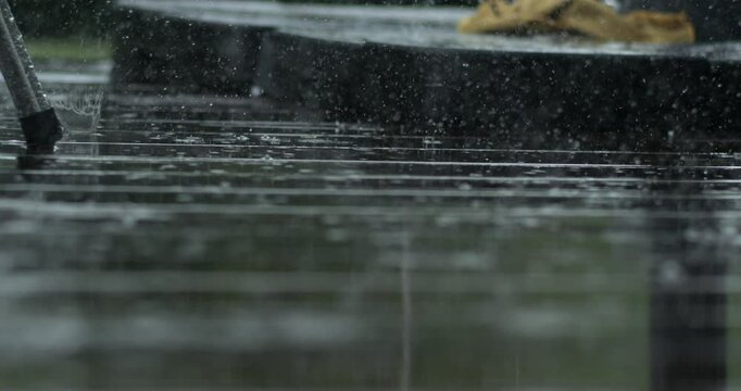 Slow motion rain captured with high speed camera bouncing off deck, with distant table and chair in background, soft focus and detailed water patterns