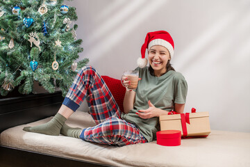 woman in santa hat and pajamas holds hot chocolate next to Christmas tre.