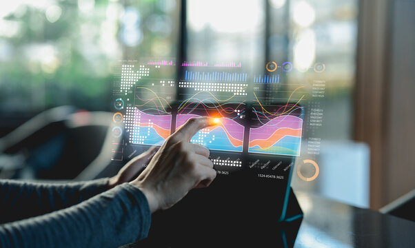 A person interacts with a transparent digital interface displaying colorful data charts and graphs inside a modern office setting.