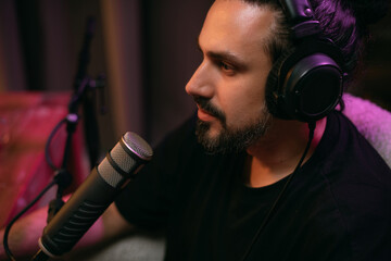 Audio podcast recording studio. A young man sits at a table in front of a microphone, recording the release of an online audio show. The host is recording the show.