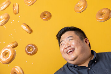 A smiling man who loves donuts. Closeup. Glazed donuts. Donuts are falling. Happiness. Obesity. Fat. Diet. Self-love. Big boy. Smiles. Yellow background.