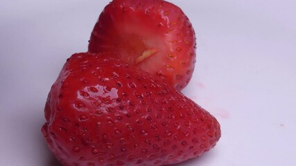 Many strawberries in a white background. At first a hand comes into frame a places a single strawberry, then places more and more berries down.