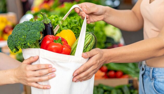 Close-up shot of person hands passing a full reusable grocery bag with vegetables