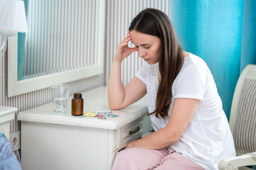 Tired woman in bedroom getting ready to take pills, glass of water and medicine placed in front of...
