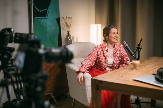 Video podcast recording studio. A conversation between a man and a woman sitting in front of microphones and cameras. The host of the podcast is interviewed about the release of a new episode.